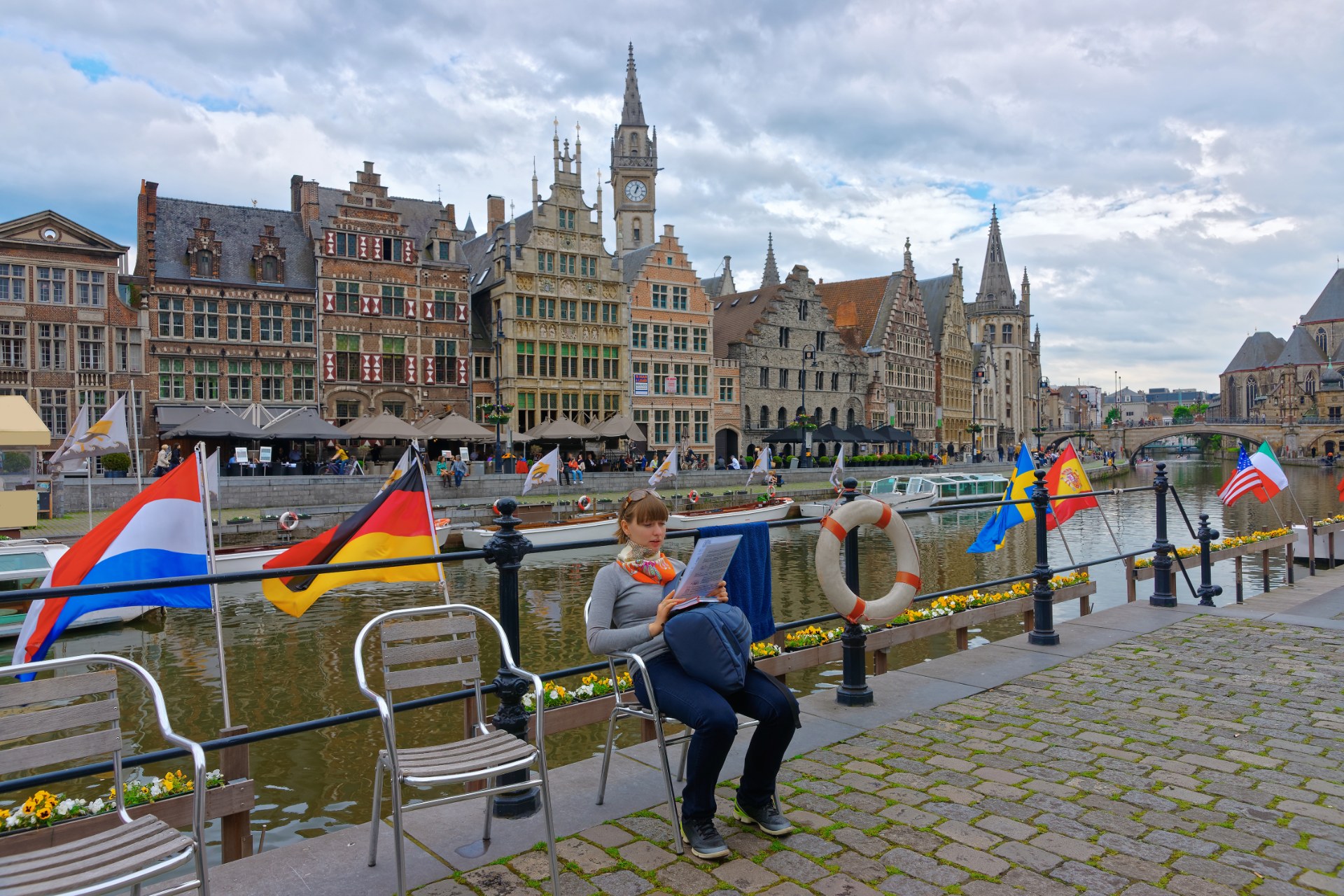 Jeune femme lisant sur le quai Korenlei à Gand, avec les maisons du Graslei en arrière-plan