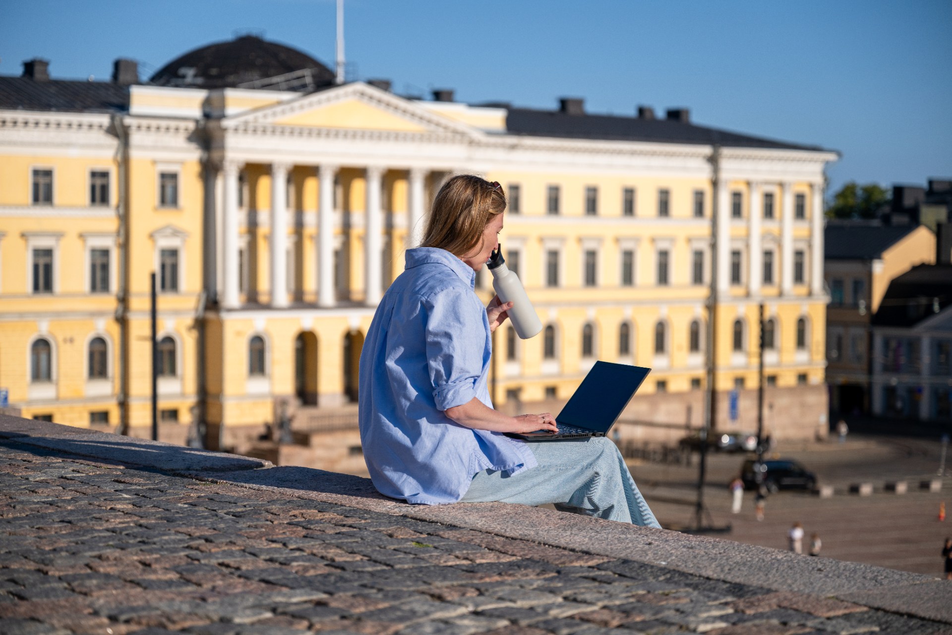 Jeune femme avec un ordinateur portable assise sur les marches de la place du Sénat à Helsinki